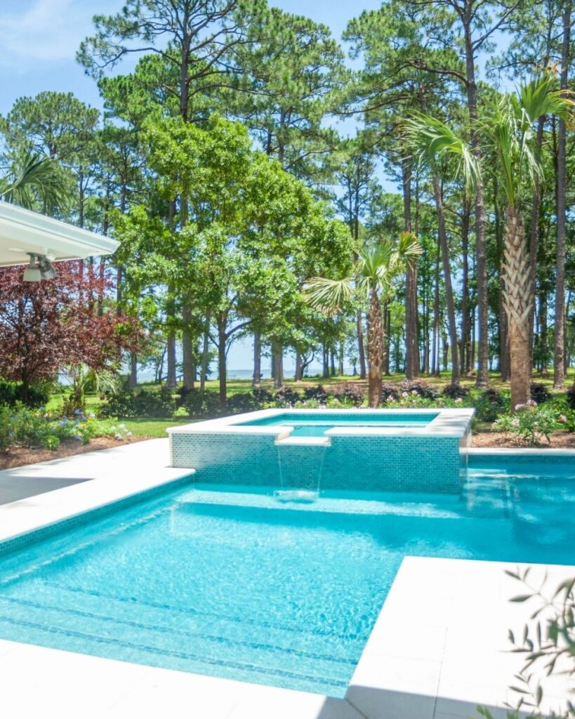 Luxury pool and spa with forest backdrop and modern white tile patio