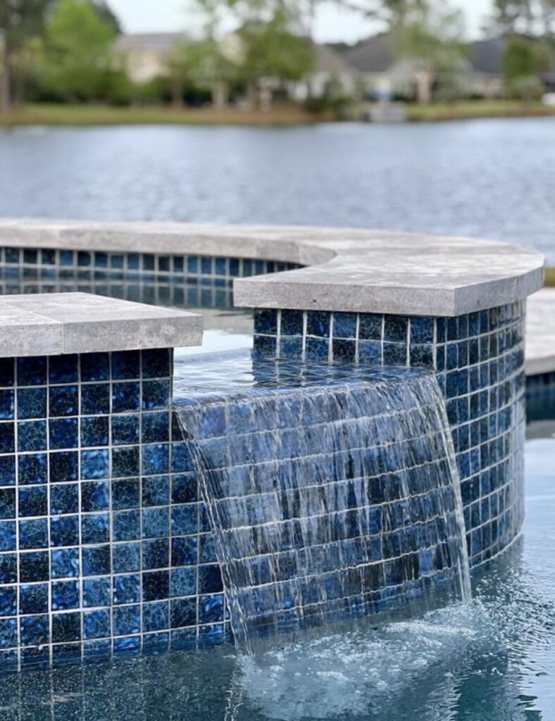 a luxurious spa spillover with a rich blue tile finish, where water gently cascades into a pristine pool, creating a serene and elegant backyard atmosphere with a scenic lake view in the background.
