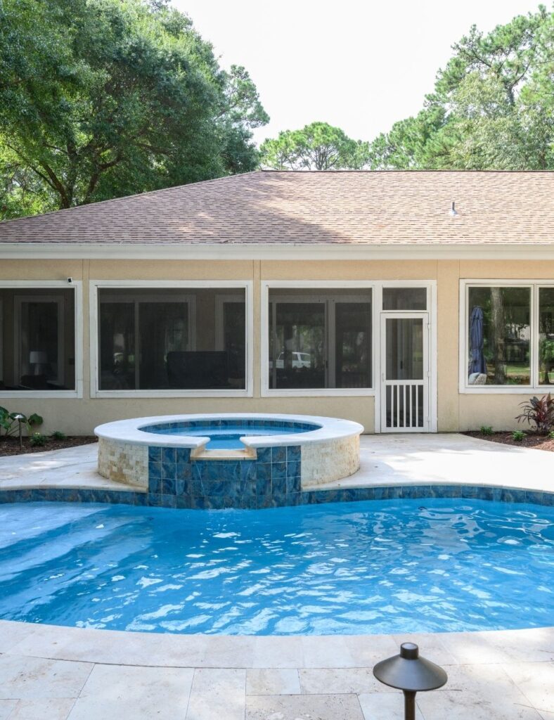 charming backyard retreat features a circular spa spilling into a petite, curved pool, surrounded by lush greenery and light-toned pavers that create a bright, serene space perfect for relaxing or entertaining