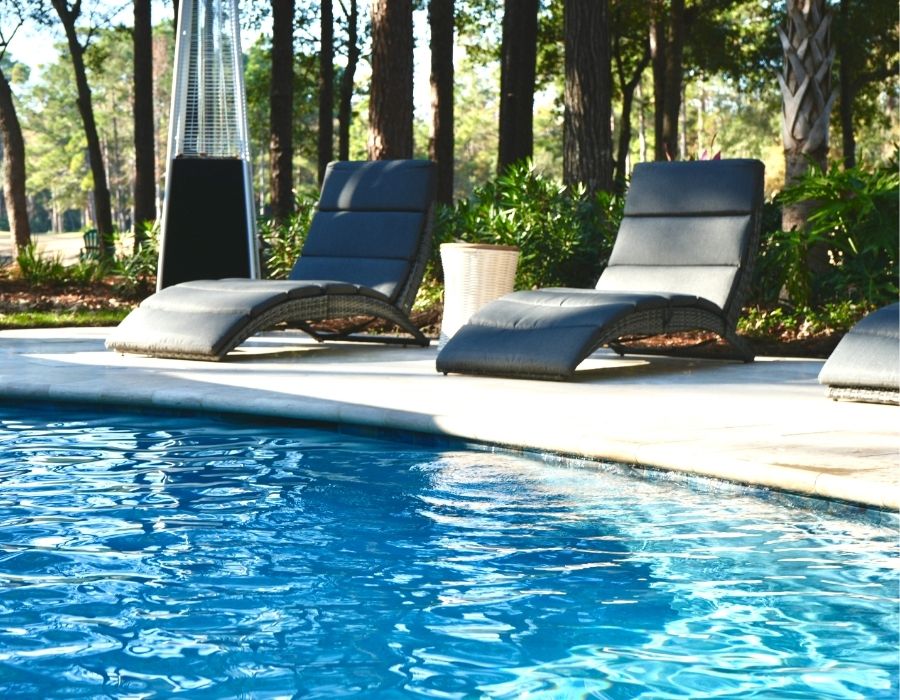 poolside scene features sleek, curved lounge chairs paired with plush cushions and surrounded by serene woodland views—perfect for soaking up the sun in total comfort and style