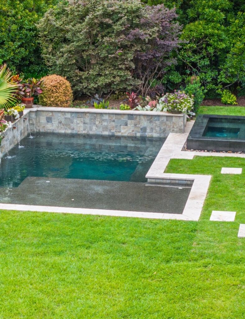 Surrounded by lush greenery and vibrant landscaping, this small rectangular pool and spa combo brings elegance and tranquility to the backyard, blending natural stone finishes with modern design for the ultimate private oasis