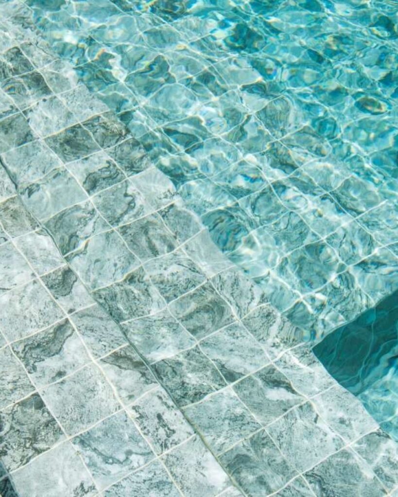 close-up of stone-tiled swimming pool steps under clear blue water